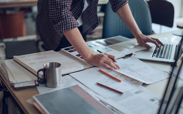 Person über Bauplan und Laptop gebeugt
