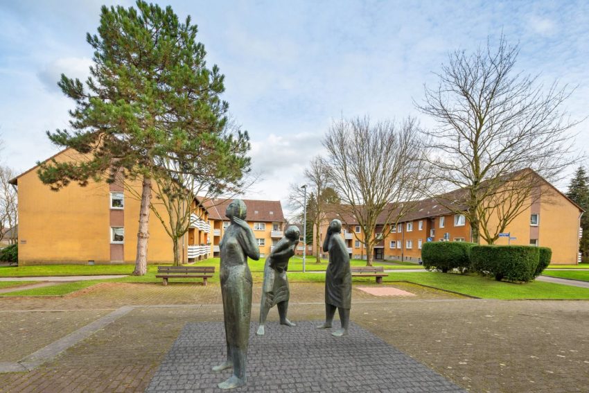 Fassade Mehrfamilienhäuser mit Grünflächen und drei Statuen im Vordergrund