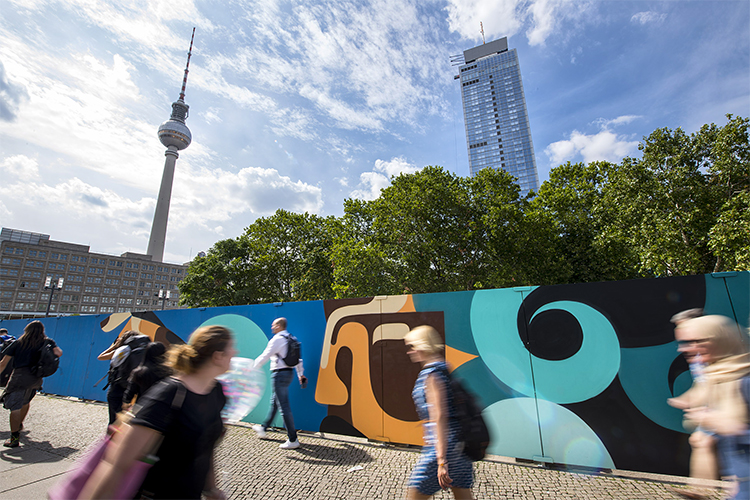 Kunstwerk auf Mauer, dahinter Hochhaus und Fernsehturm
