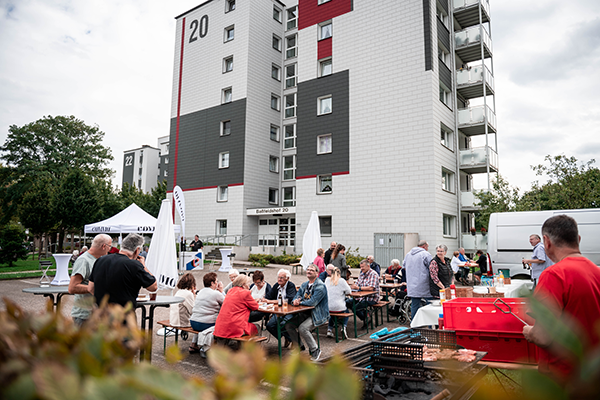 Menschen an Bierzelttischen vor Mehrfamilienhaus
