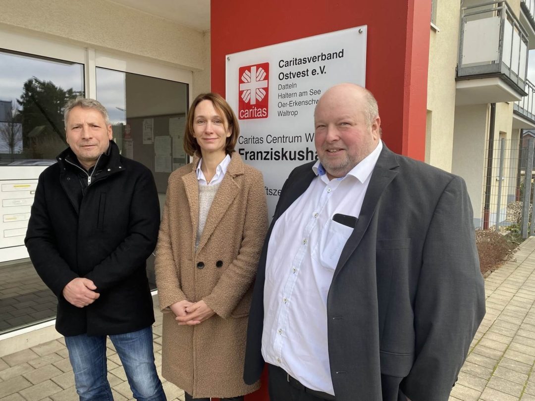 drei Personen vor Caritas-Schild