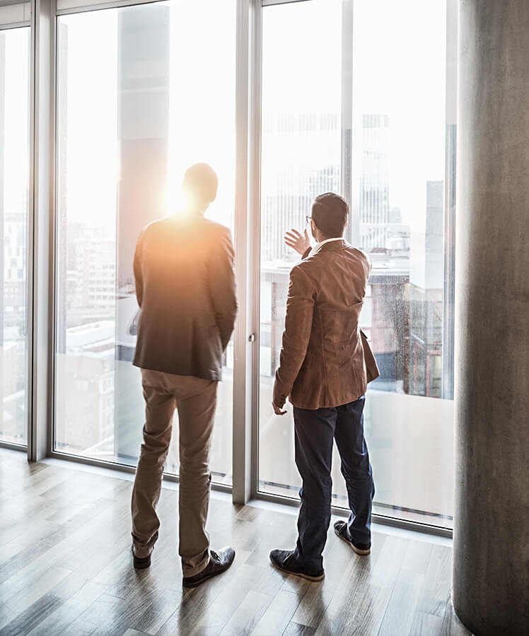 Zwei Männer schauen durch große Glasfassade nach draußen über die Stadt
