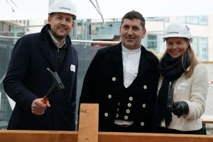 Zimmermann und zwei Personen mit Bauhelm und Hammer