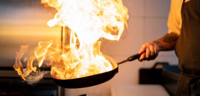 Ein Koch hält eine brennende Pfanne in der Hand