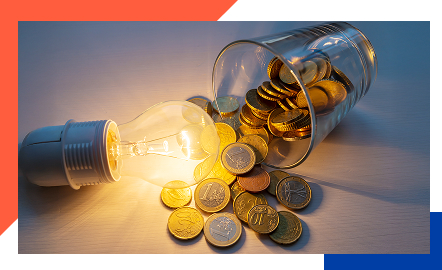 Ein umgekipptes Glas mit Münzen und daneben eine leuchtende Glühbirne