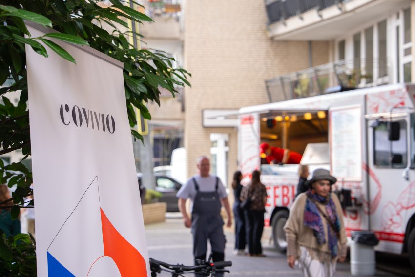 Aufsteller mit dem Schriftzug 'COVIVIO', im Hintergrund ein Foodtruck mit Menschen davor.