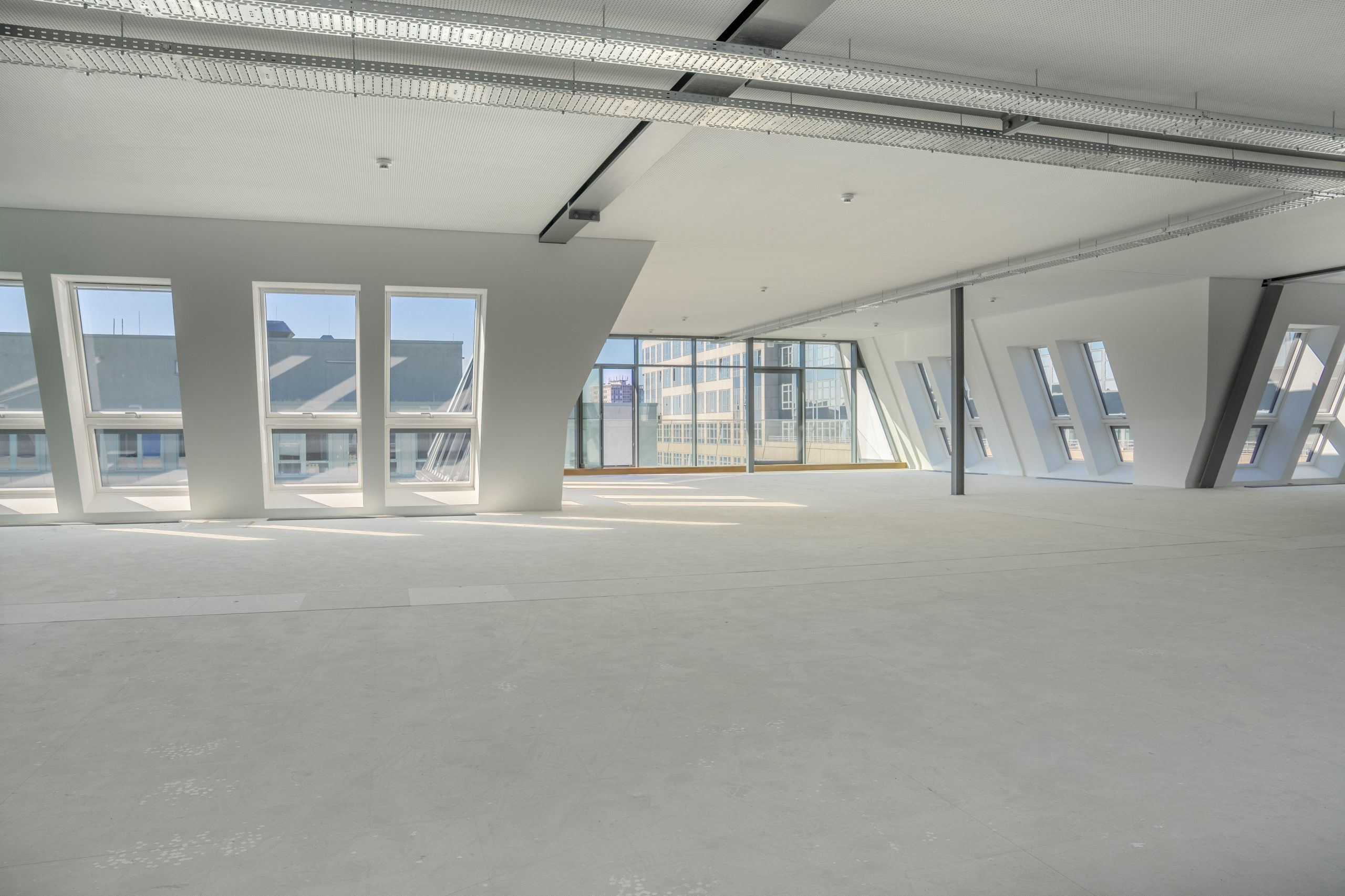 Heller Büroraum mit großen Fenstern und sichtbaren Deckeninstallationen.