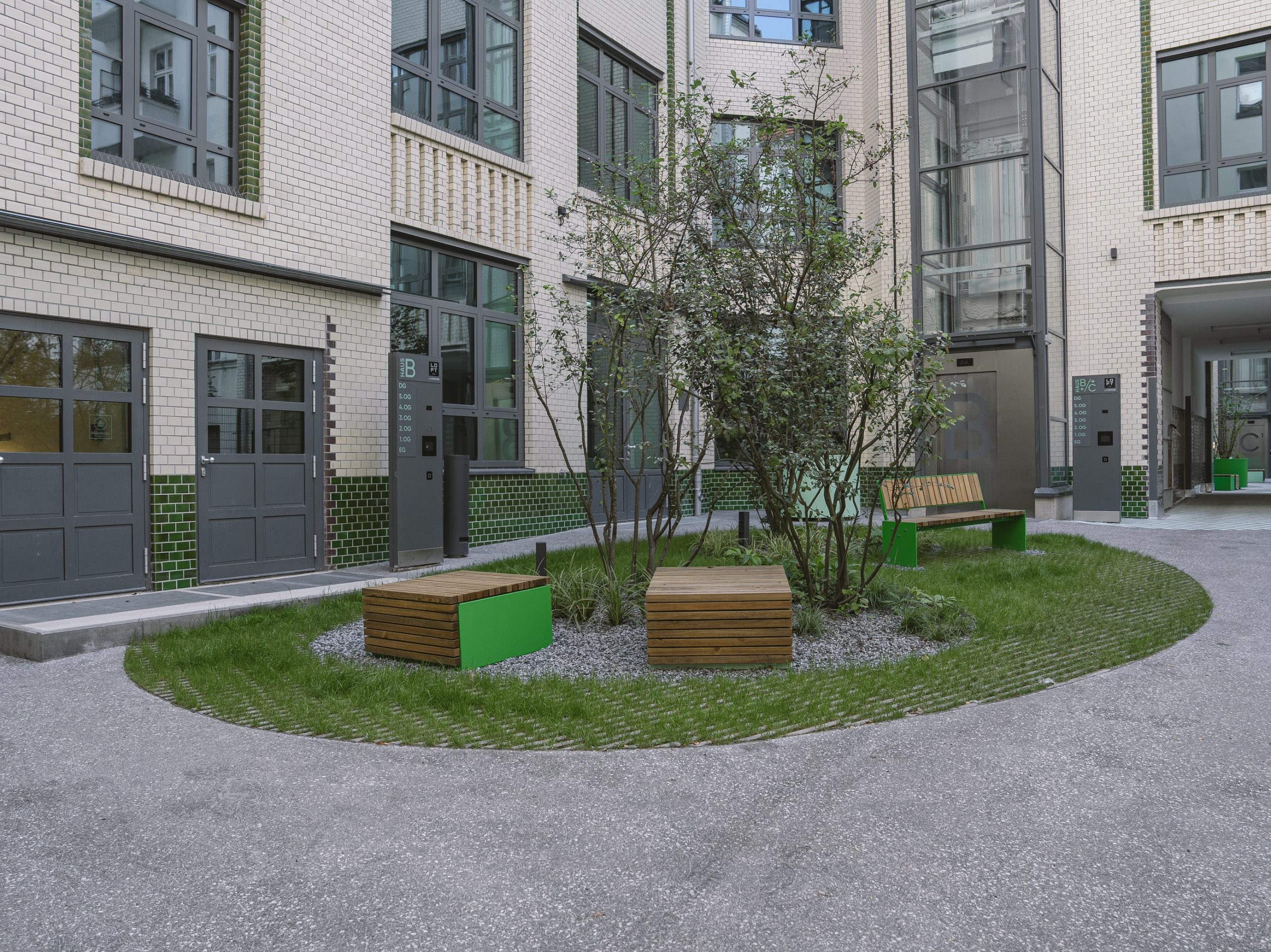 Innenhof mit Sitzbänken und Bäumen, umgeben von mehrstöckigem Gebäude mit hellen Fassaden und Fenstern